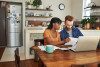 Young couple at kitchen table with papers, calculator, and laptop