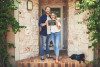 Young couple standing in front of their new home holding a chalkboard with "first home" written on it